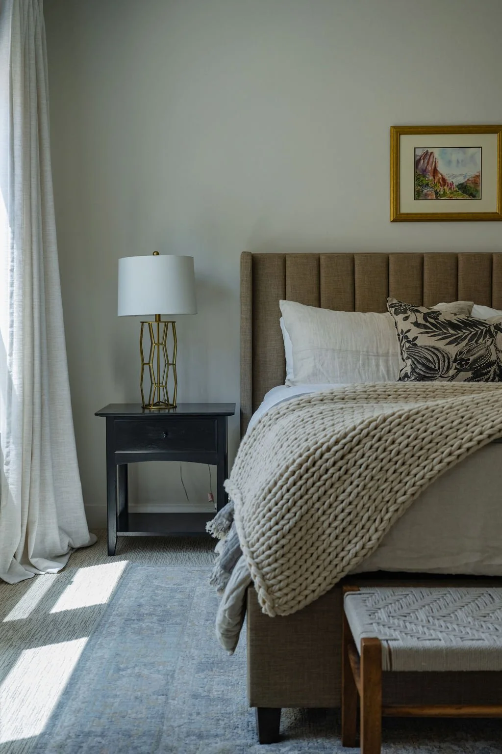 Warm and inviting bedroom corner with soft linen drapes, a black nightstand, and a gold table lamp for a refined style.