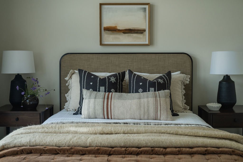 Bohemian-inspired bedroom with a linen-upholstered bed, black and white patterned pillows, and a neutral abstract painting.