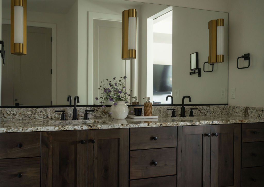 Elegant bathroom with a dark wood vanity, granite countertops, black fixtures, and modern gold sconces for a luxurious touch