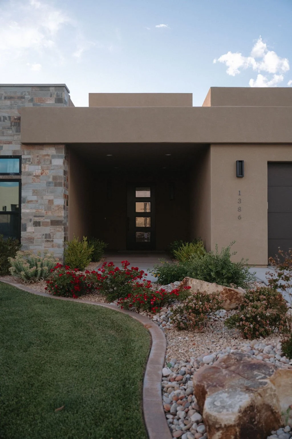 Stylish entryway of a modern home with a deep-set front door, warm stone details, and desert-inspired plantings.