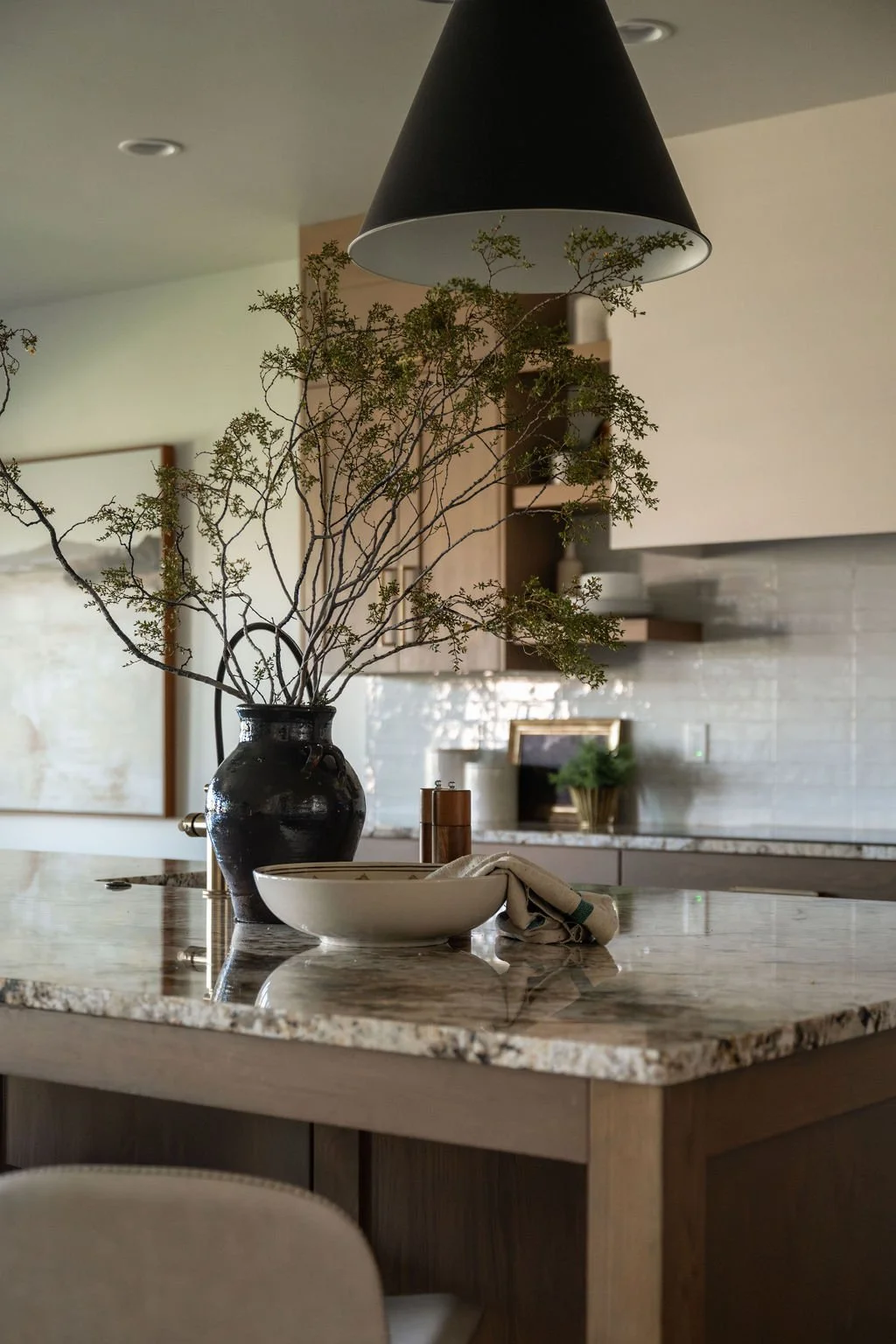 Kitchen island styled with a black vase and branches, neutral dishware, and a textured backsplash adding depth to the design.
