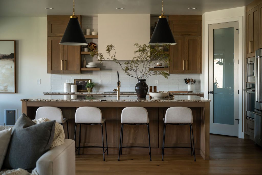 Luxury kitchen with black and gold pendant lighting, warm wood cabinetry, and a large island with light upholstered barstools.