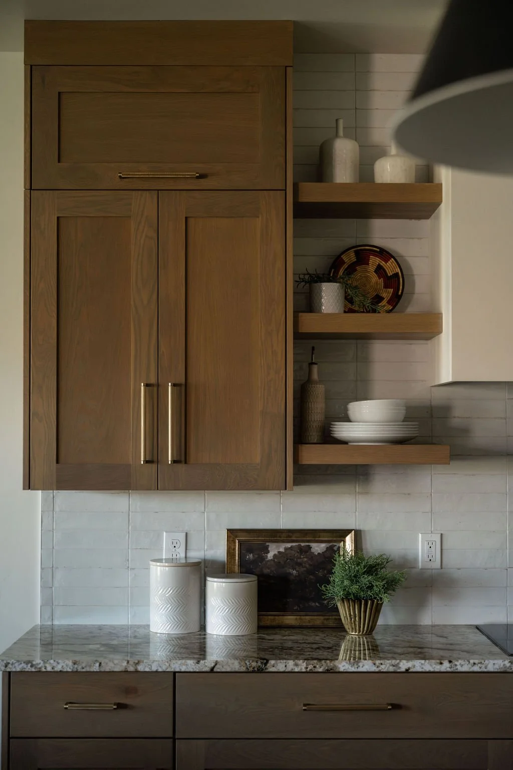 Modern kitchen cabinetry with a mix of closed storage and open shelving, displaying neutral dishware and organic decor accents.