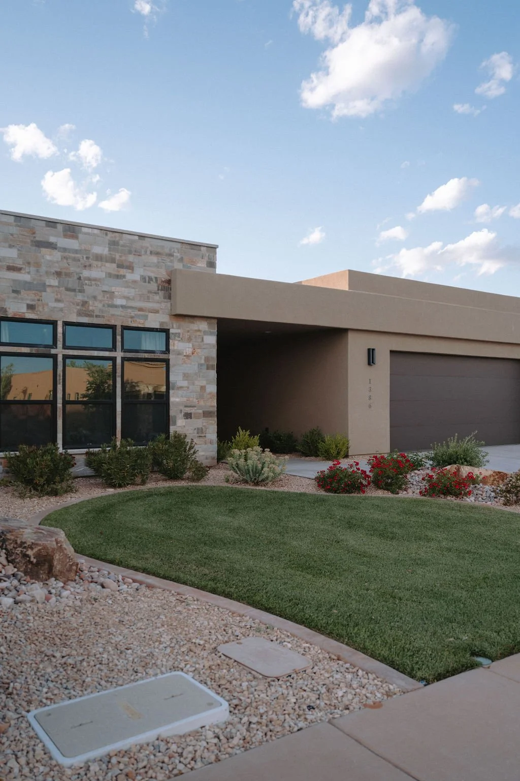 Modern home exterior in Saint George, Utah, featuring stone and stucco facade, drought-tolerant landscaping, and sleek black-framed windows.
