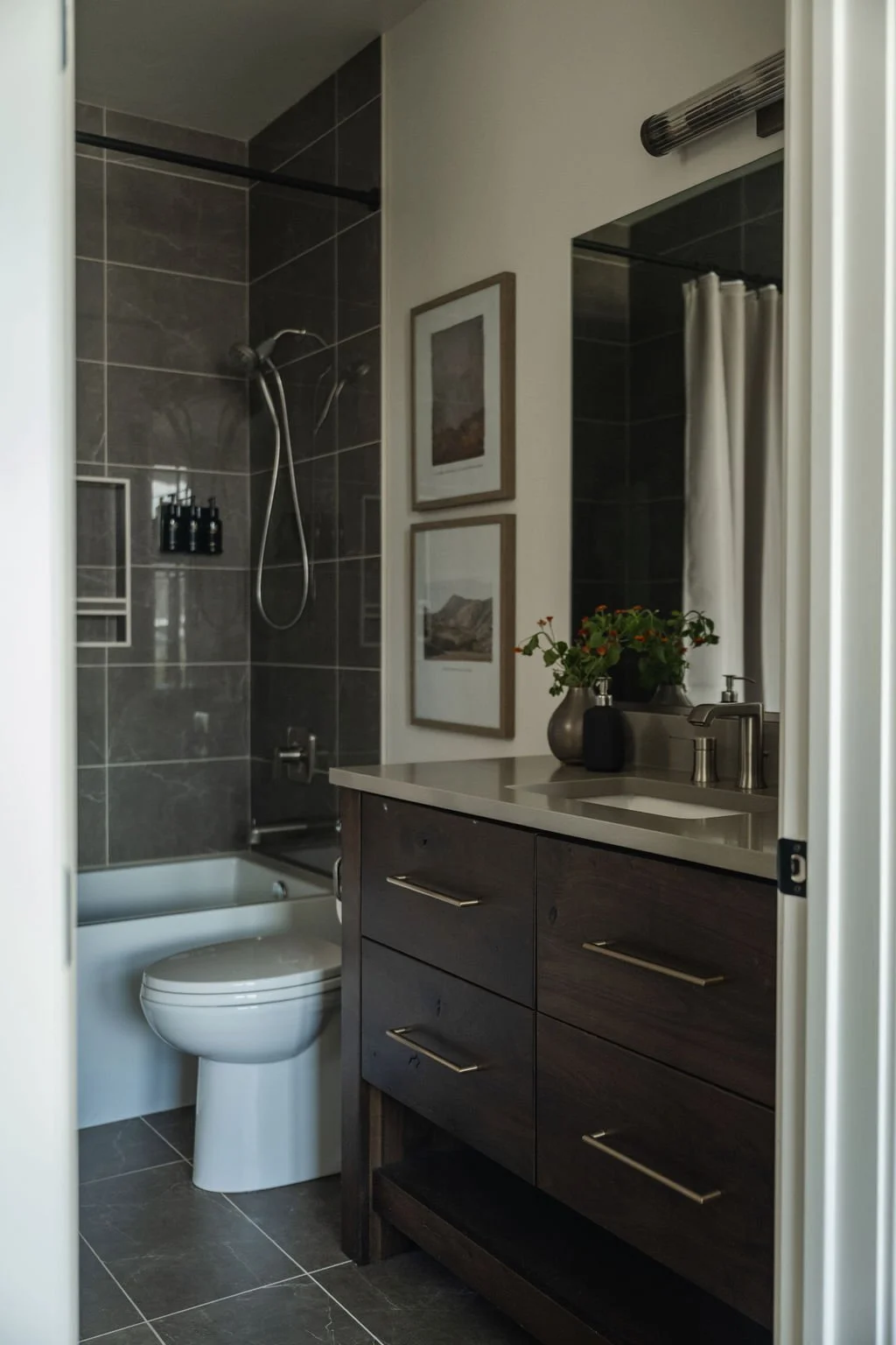 Modern bathroom with dark tile shower, sleek vanity with gold hardware, and framed artwork for a refined look.