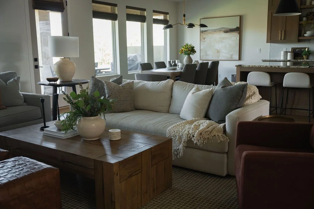 Open-concept living and dining space with large windows, a plush sectional, warm wood accents, and modern pendant lighting.