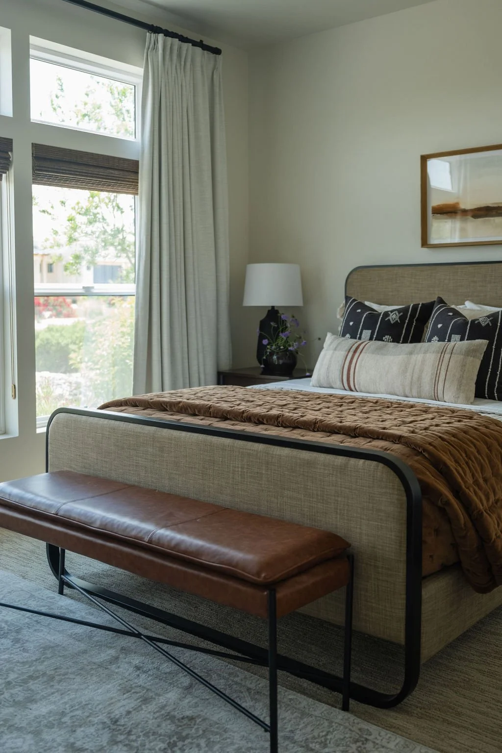Modern bedroom with a woven-texture bed frame, layered bedding in earthy tones, and a leather bench at the foot of the bed.