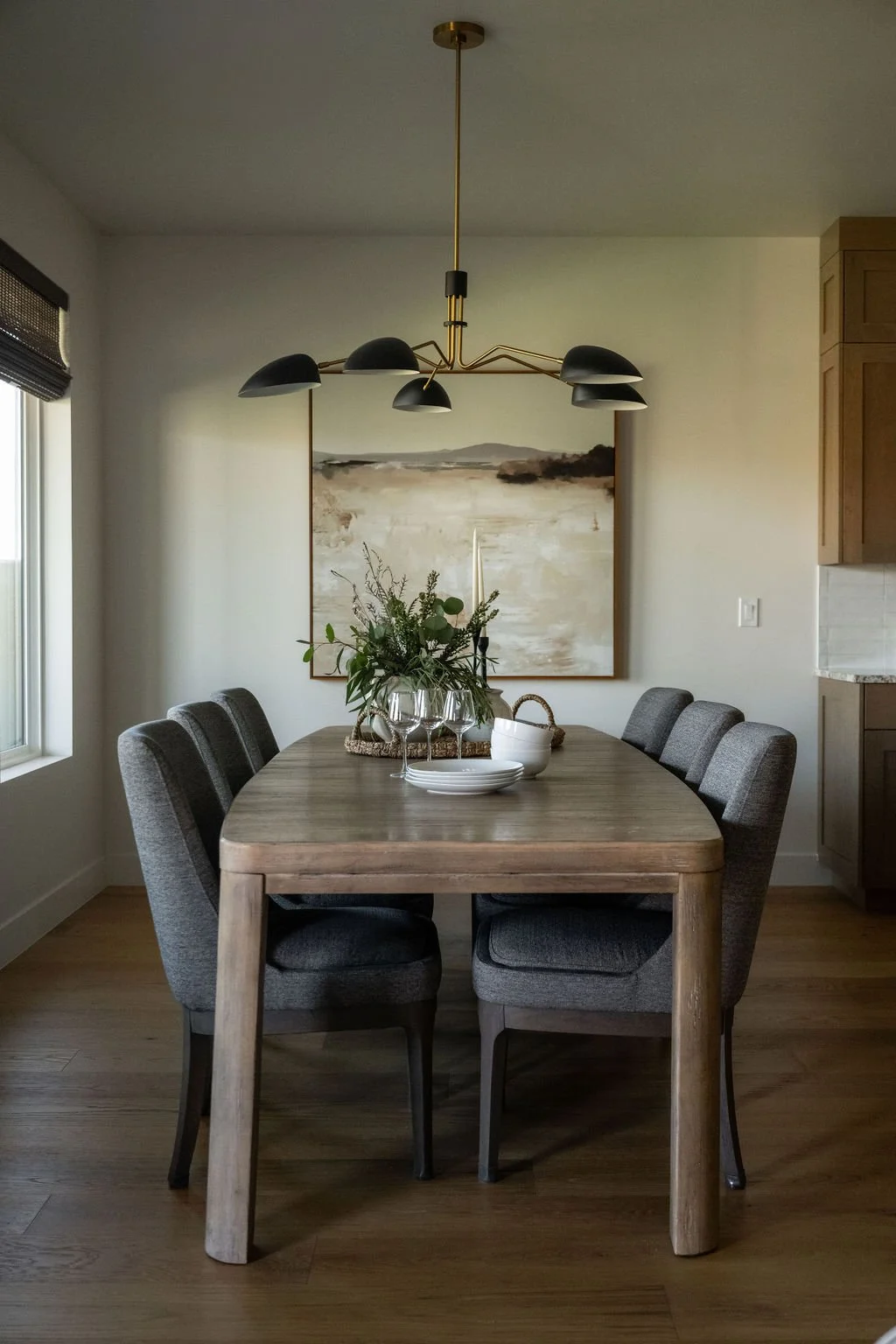 Sophisticated dining area with a wood table, black upholstered chairs, a gold statement chandelier, and a large framed desert landscape artwork.