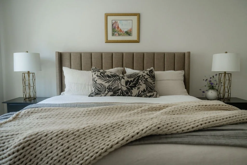 Neutral bedroom with an upholstered headboard, cozy knit blanket, and framed landscape artwork for a serene retreat.