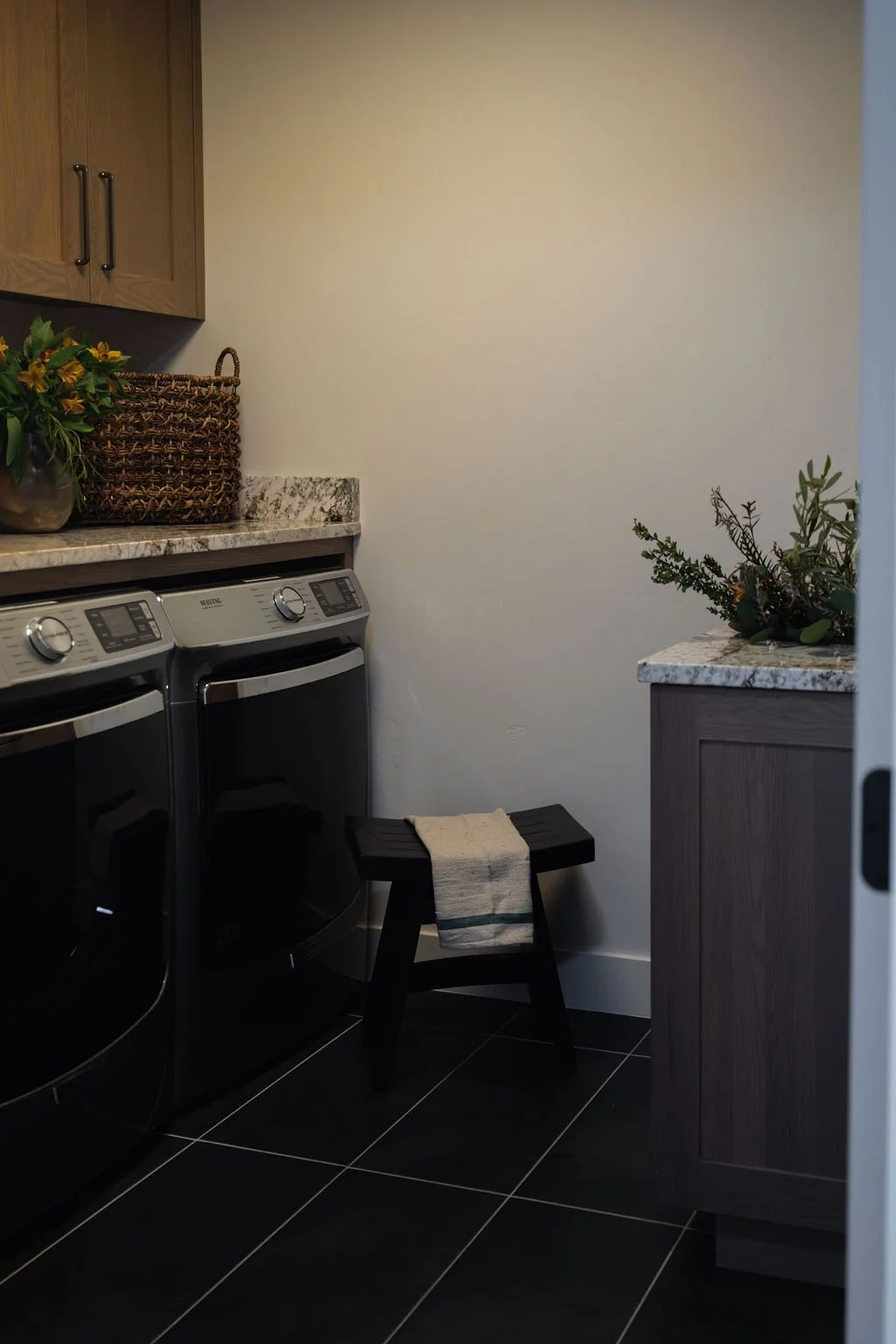 Stylish laundry room with wood cabinetry, black washer and dryer, and natural decor elements creating a functional yet beautiful space.
