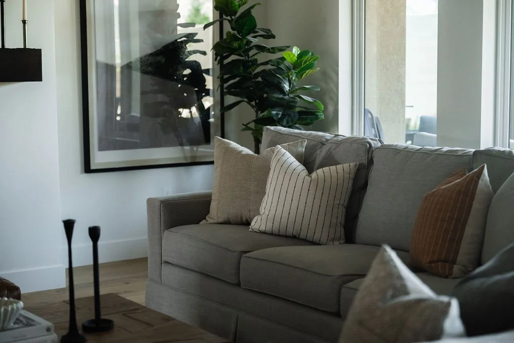 Cozy seating area with a gray sofa, striped accent pillows, and a large framed abstract artwork, styled with natural light.