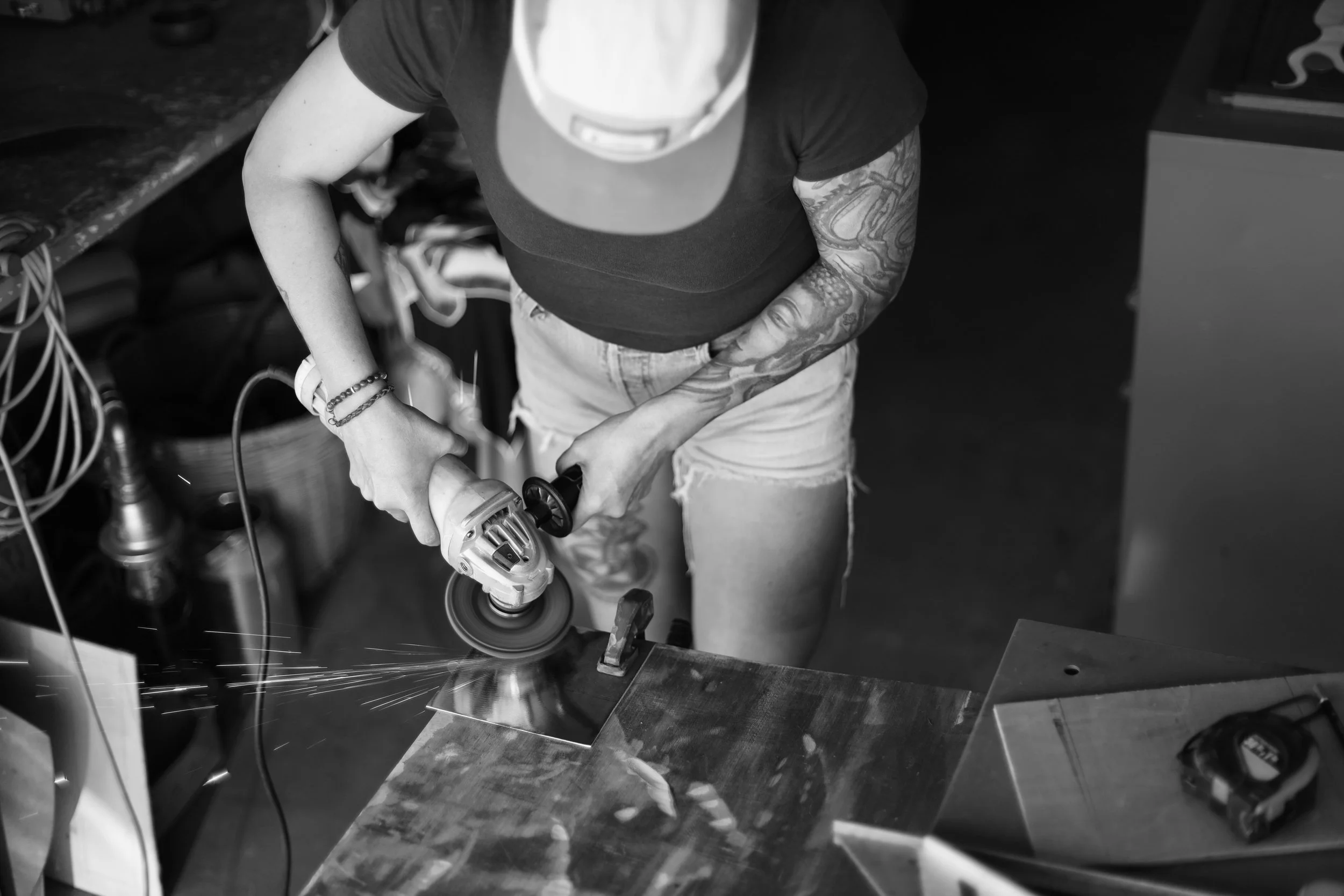 Person using an angle grinder to cut a piece of metal in a workshop, sparks flying.