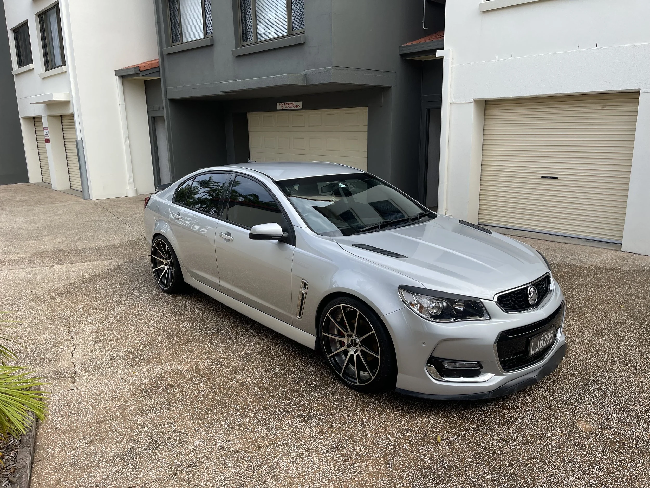 Silver sedan parked in front of a modern residential building with three garage doors, some with partitioned windows, and a pebble-textured driveway.