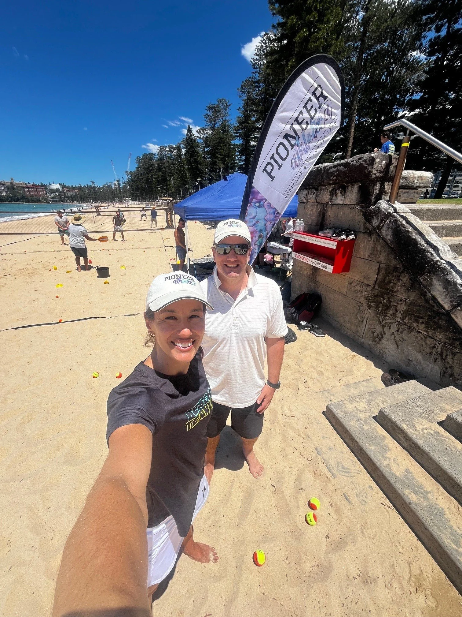 female and male beach tennis coaches smiling with hats on Manly Beach playing beach tennis team building