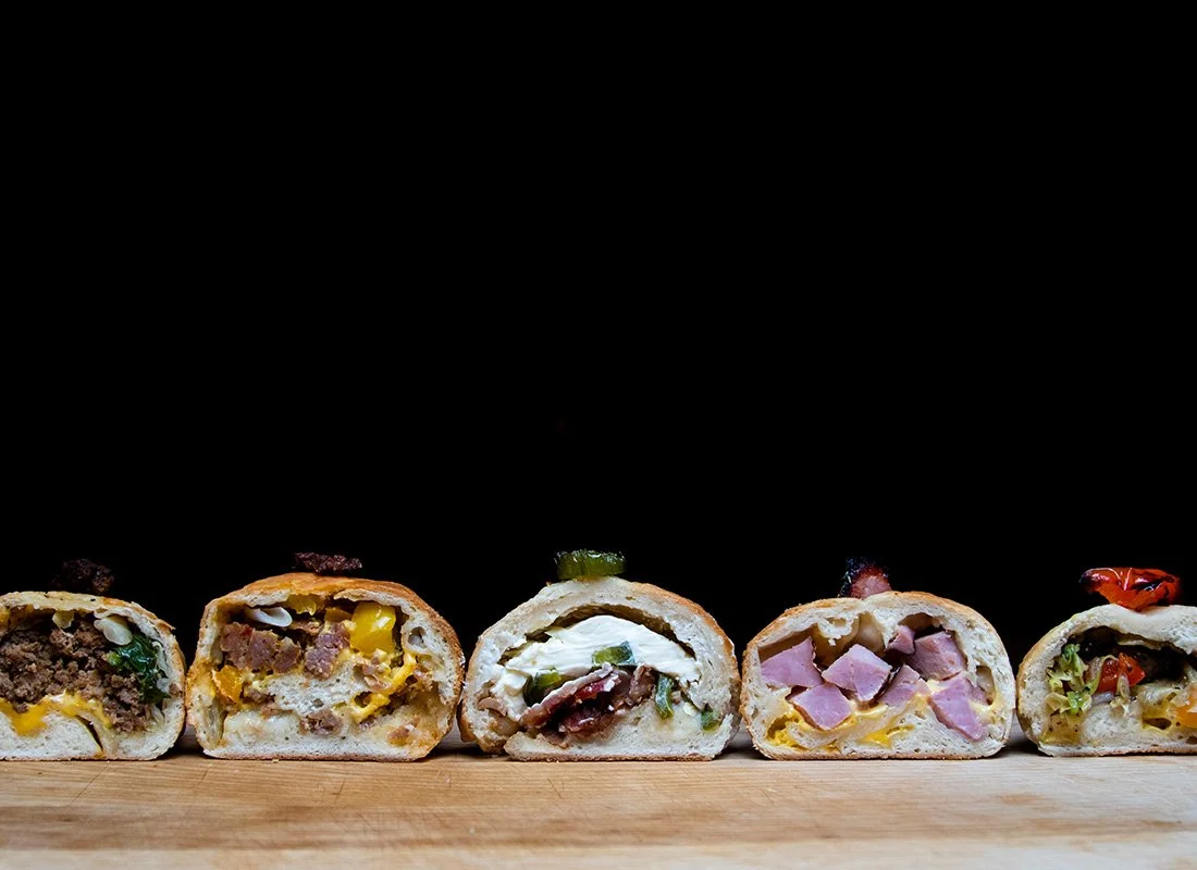 Five different stuffed bread rolls with various fillings, lined up on a wooden surface with a black background.