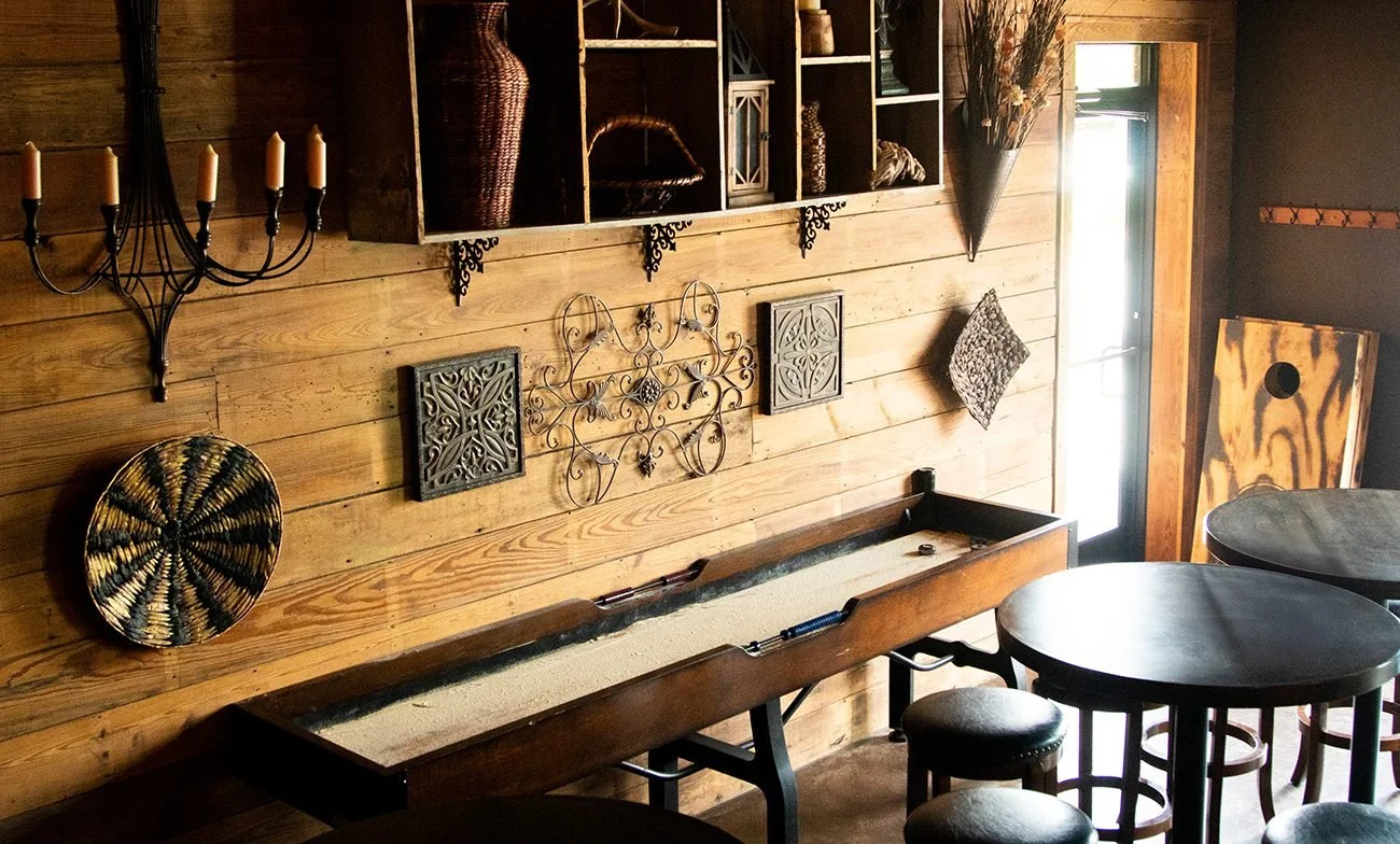 Interior of a cozy room with wooden walls, decorative wall art, a long sand-filled game tray, and round tables with stools.