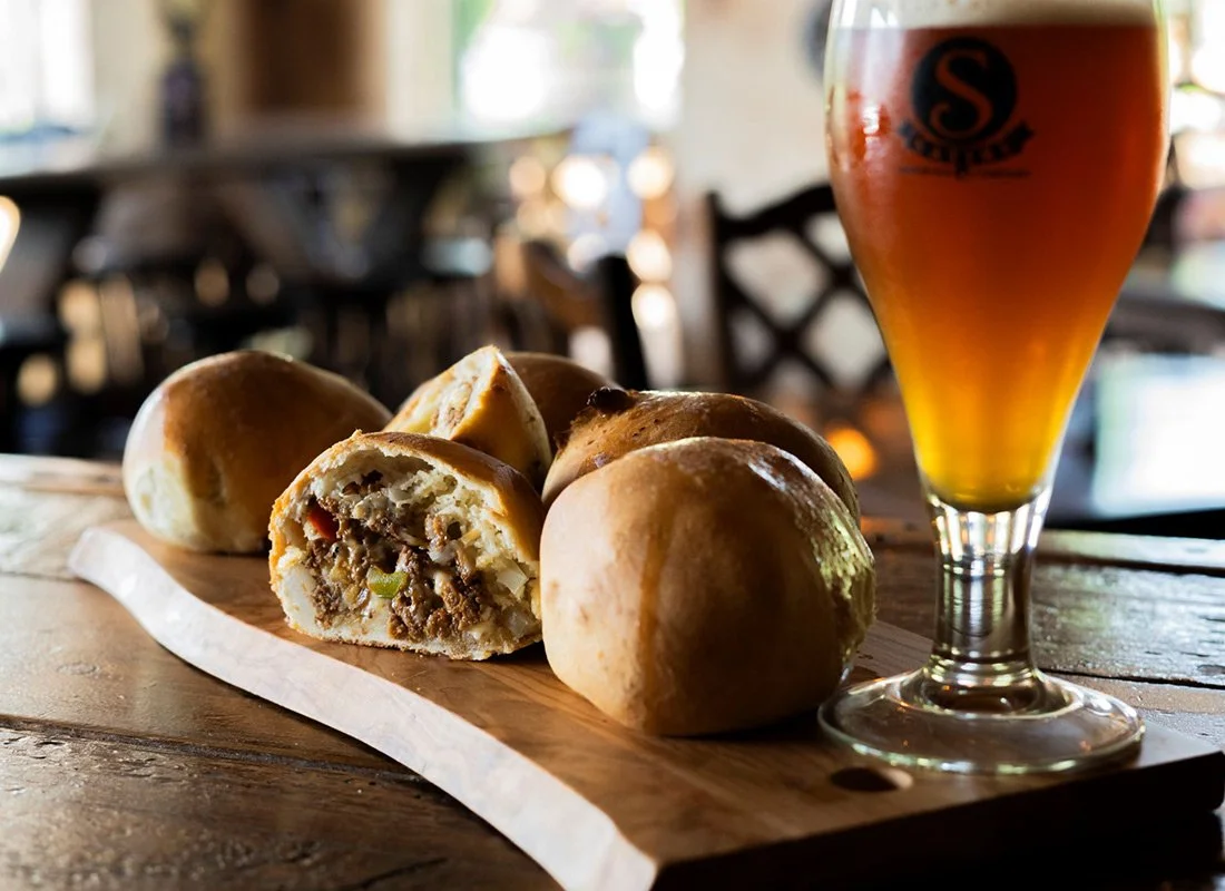 Meat and vegetable-filled bread rolls on a wooden serving board with a glass of beer.