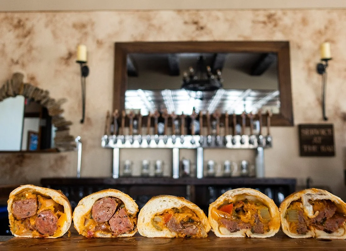 Five sausage and vegetable stuffed pastries on a wooden surface with a rustic restaurant interior in the background.