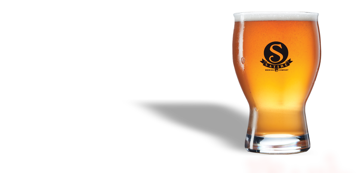 A pint glass filled with amber-colored beer with a white foam head, featuring a black logo with an orange 'S' and the word 'SATIRE' on it.