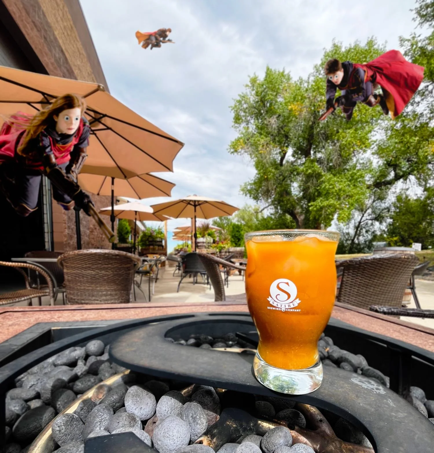 A glass of iced tea on a table at an outdoor patio, with two people dressed as Harry Potter and Hermione flying through the sky in the background.
