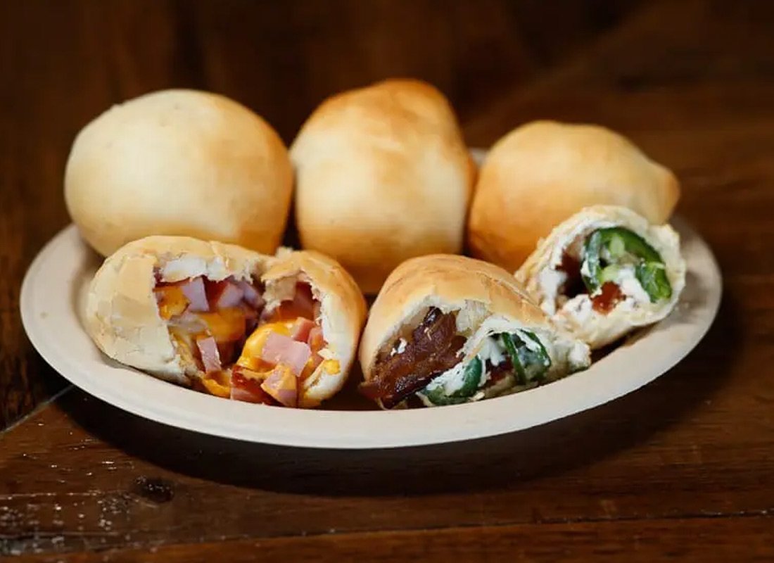 Plate of Chinese steamed buns with various fillings, some cut open showing meat, vegetables, and sauces