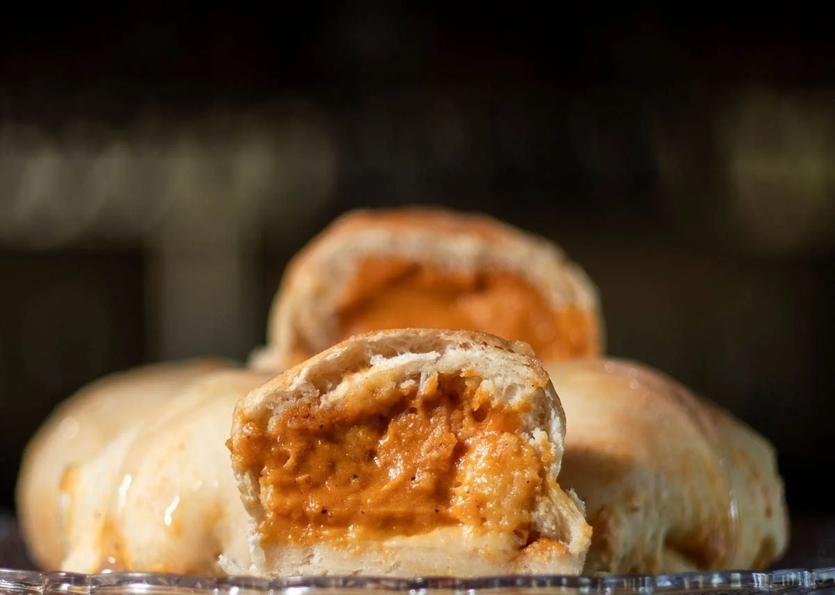 Close-up of baked empanadas with golden crust filled with a savory filling, placed on a glass dish