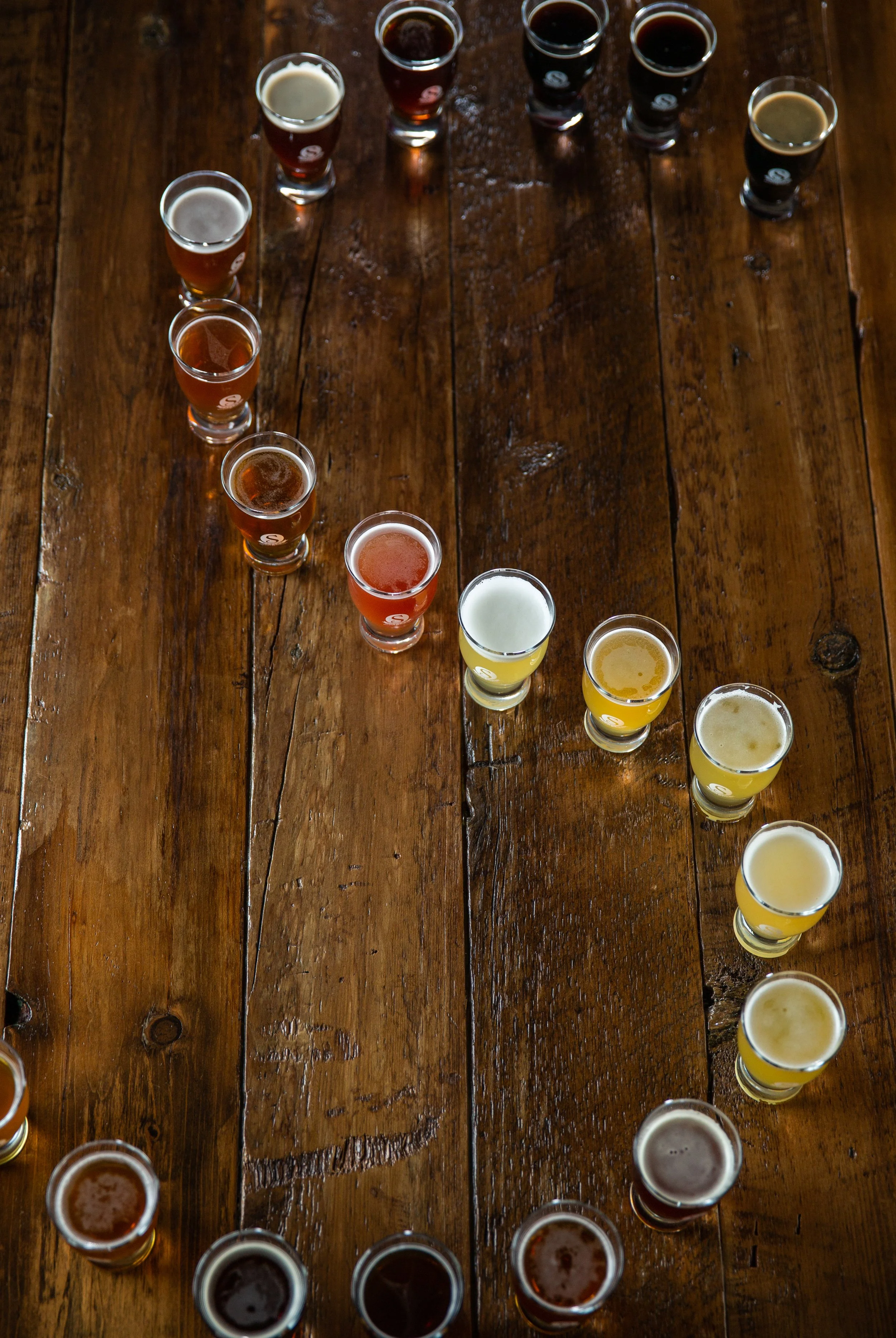 Multiple samples of beer in small glasses arranged on a wooden table.