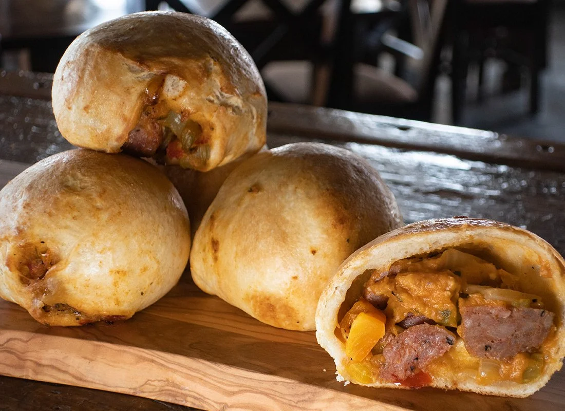 Four baked bread rolls, with two of them cut open to reveal a filling of meat, vegetables, and sauce.
