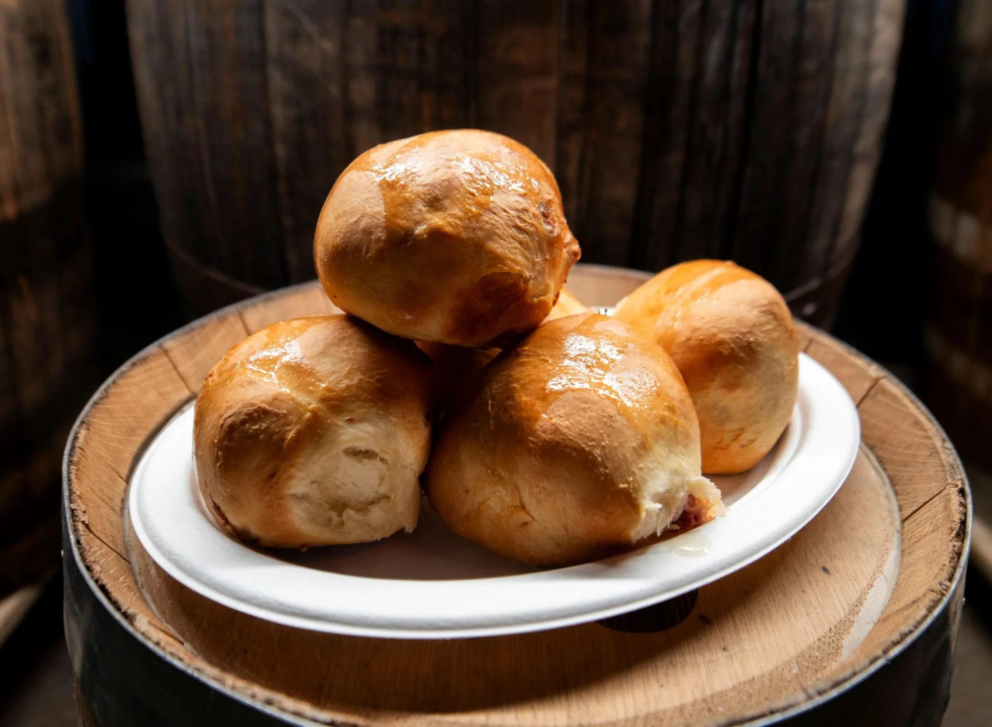 Baked bread rolls on a white plate inside a wooden bowl with a rustic wooden background.