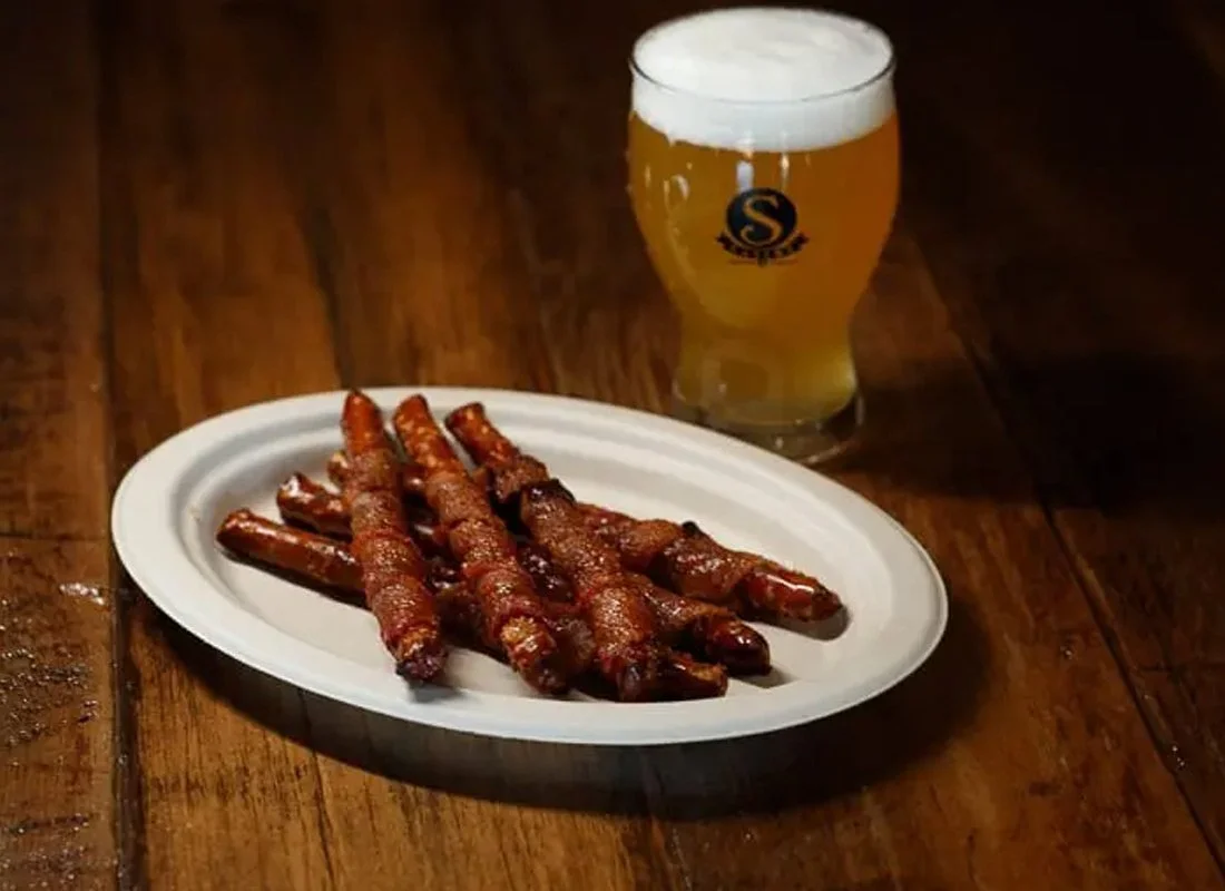Plate of cooked bacon-wrapped jalapeño peppers and a glass of beer on a wooden table.
