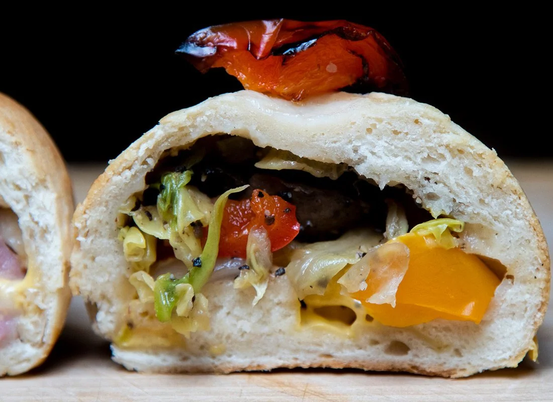 Close-up of a vegetable-filled bread roll with roasted tomato on top.