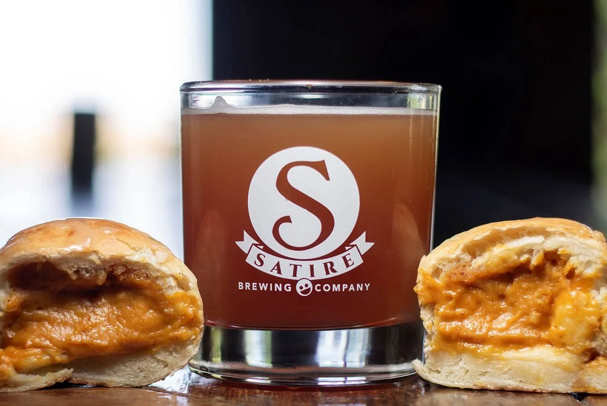 A glass of beer with the Saturn Brewing Company logo, placed between two bread rolls filled with melted cheese and peanut butter.