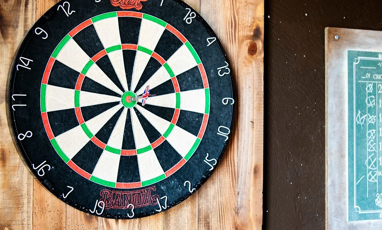 A dartboard mounted on a wooden wall with a small British flag stuck into the bullseye.