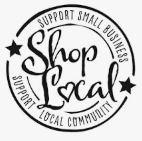 A circular black and white logo with the words 'Shop Local' in the center. The surrounding text reads 'Support Small Business' and 'Support Local Community'. There are two black stars on either side of the circle.