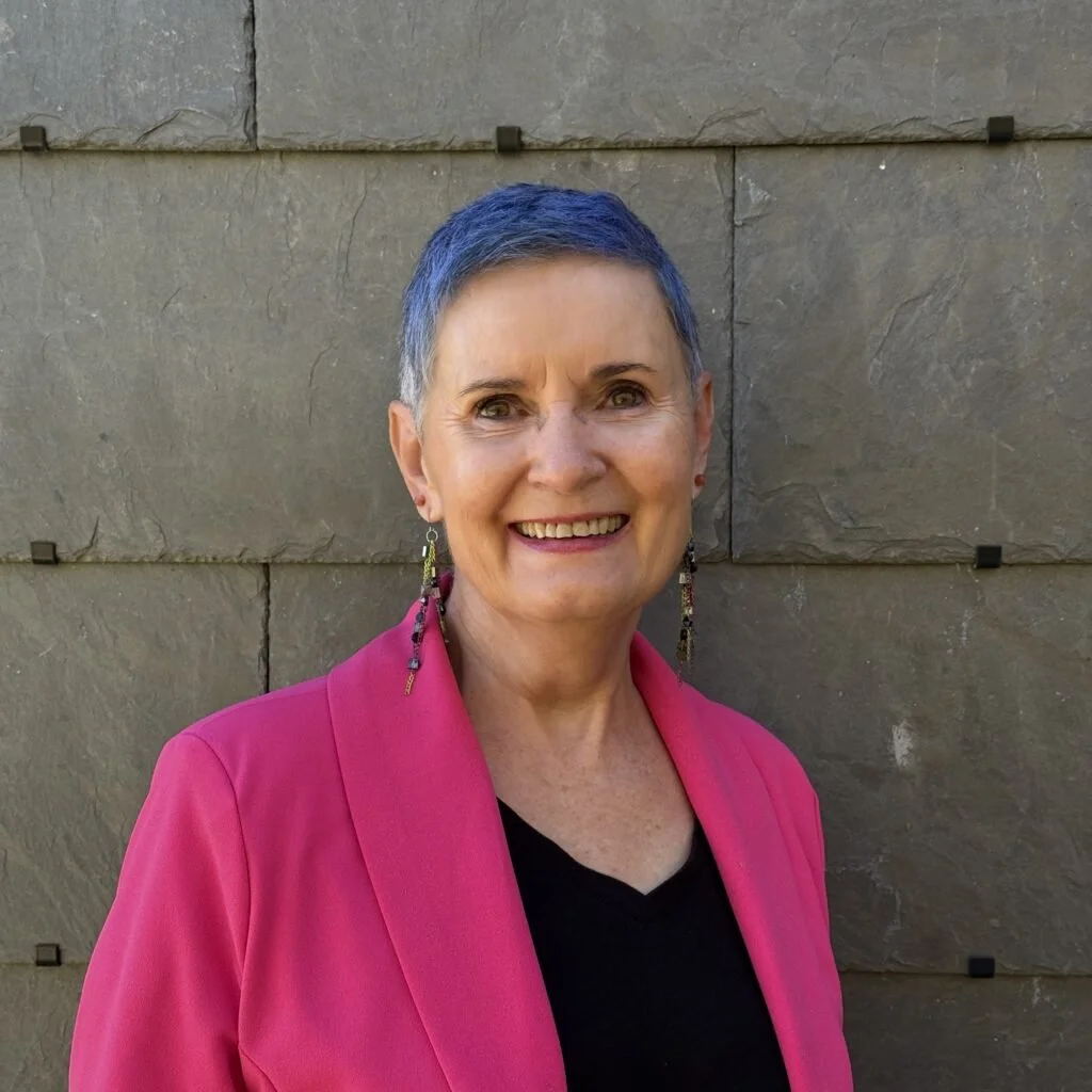 A picture of Carolyn, a white woman with blue hair in a pink jacket.