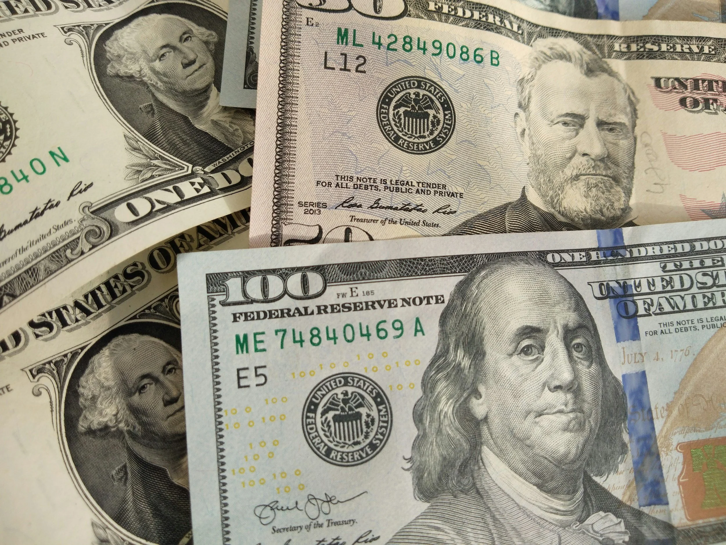 Close-up of various U.S. dollar bills, including $100 and $20 notes, overlapping each other.