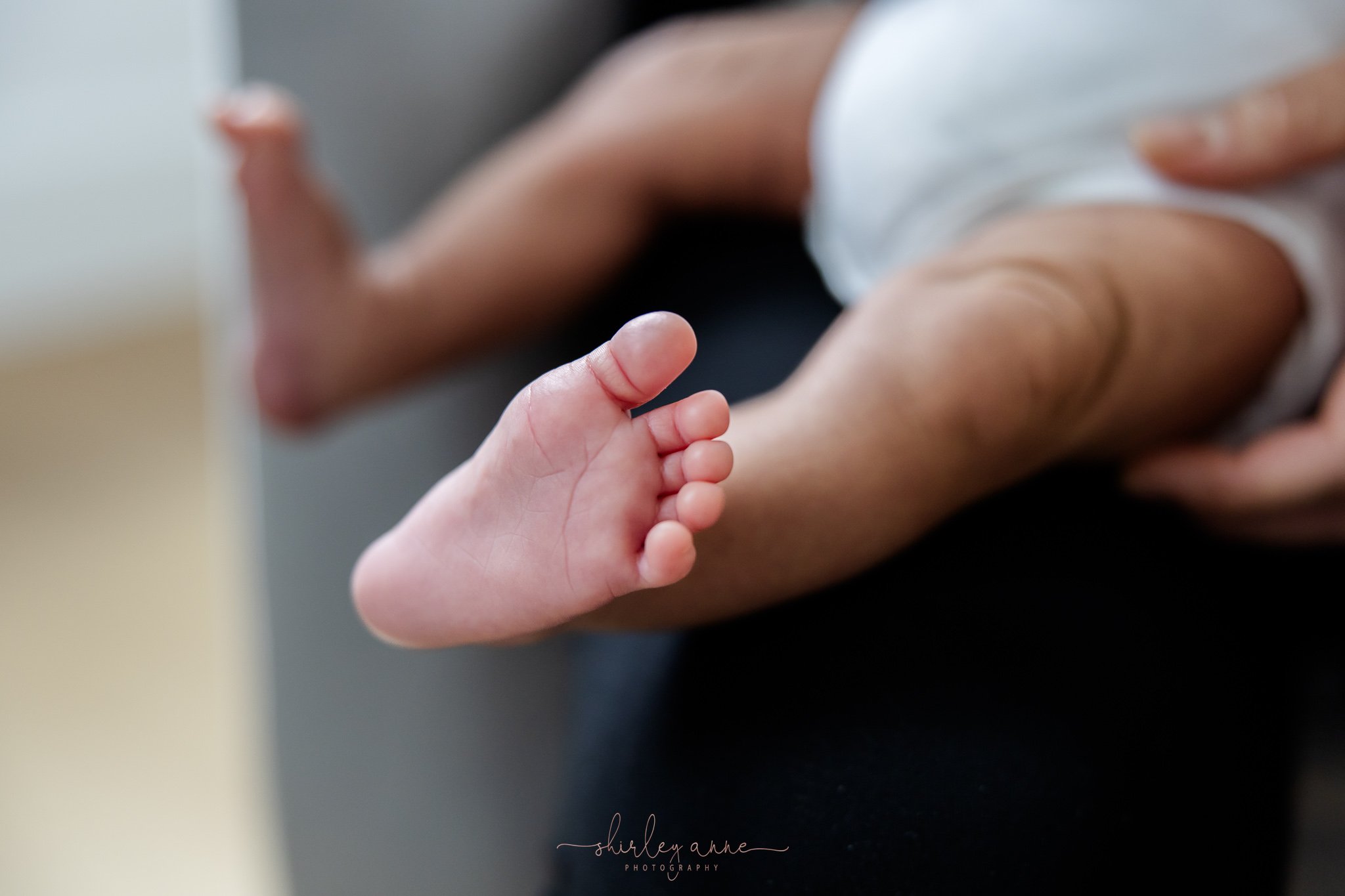Close-up of tiny baby's hand holding an adult's finger, focus on baby's hand, blurred background. Boston family photographer, Lowell family photographer, Massachusetts newborn photographer, family photographer Lowell MA, lifestyle photographer