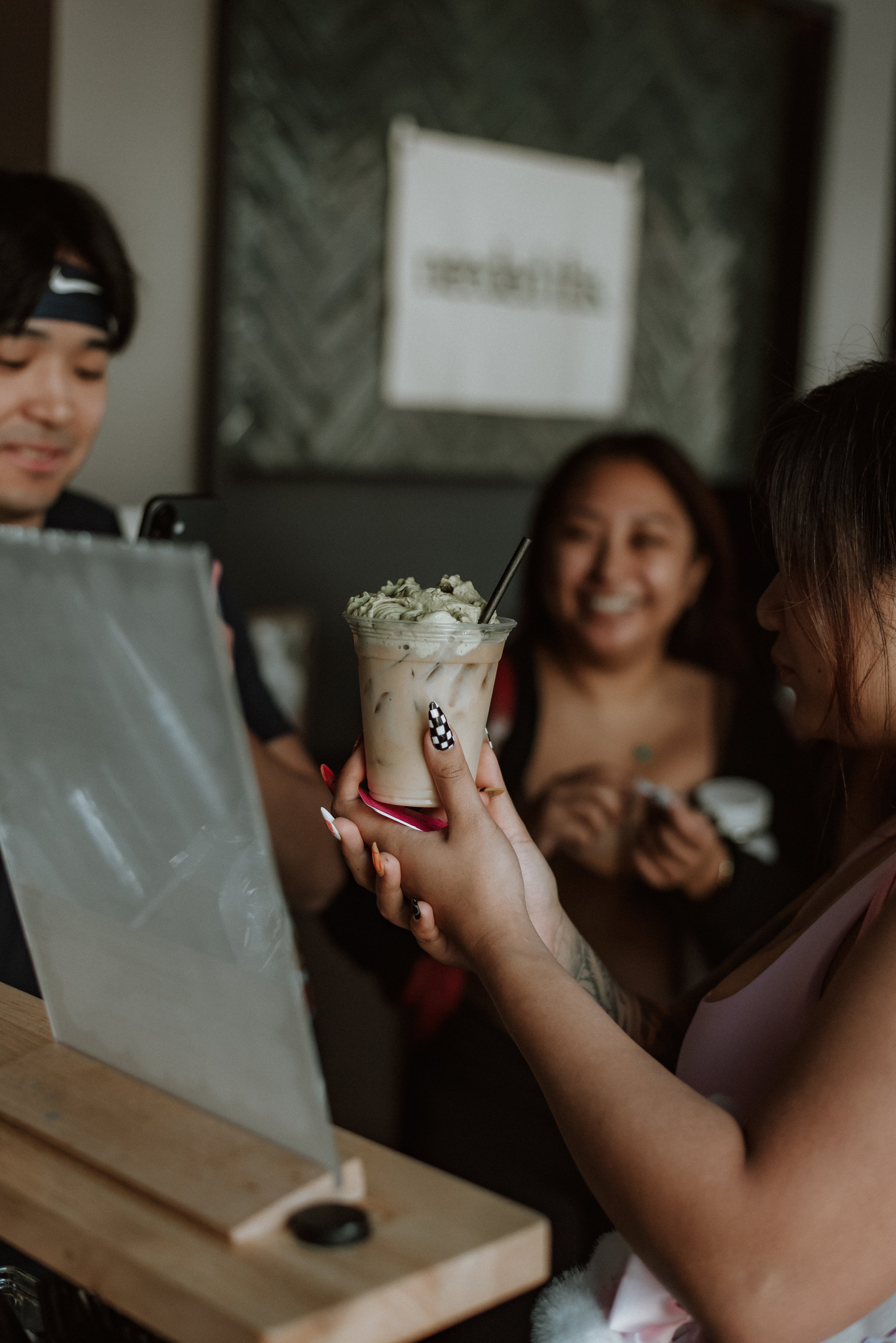 a woman holding a coffee with matcha foam while friends gather around her to enjoy the company