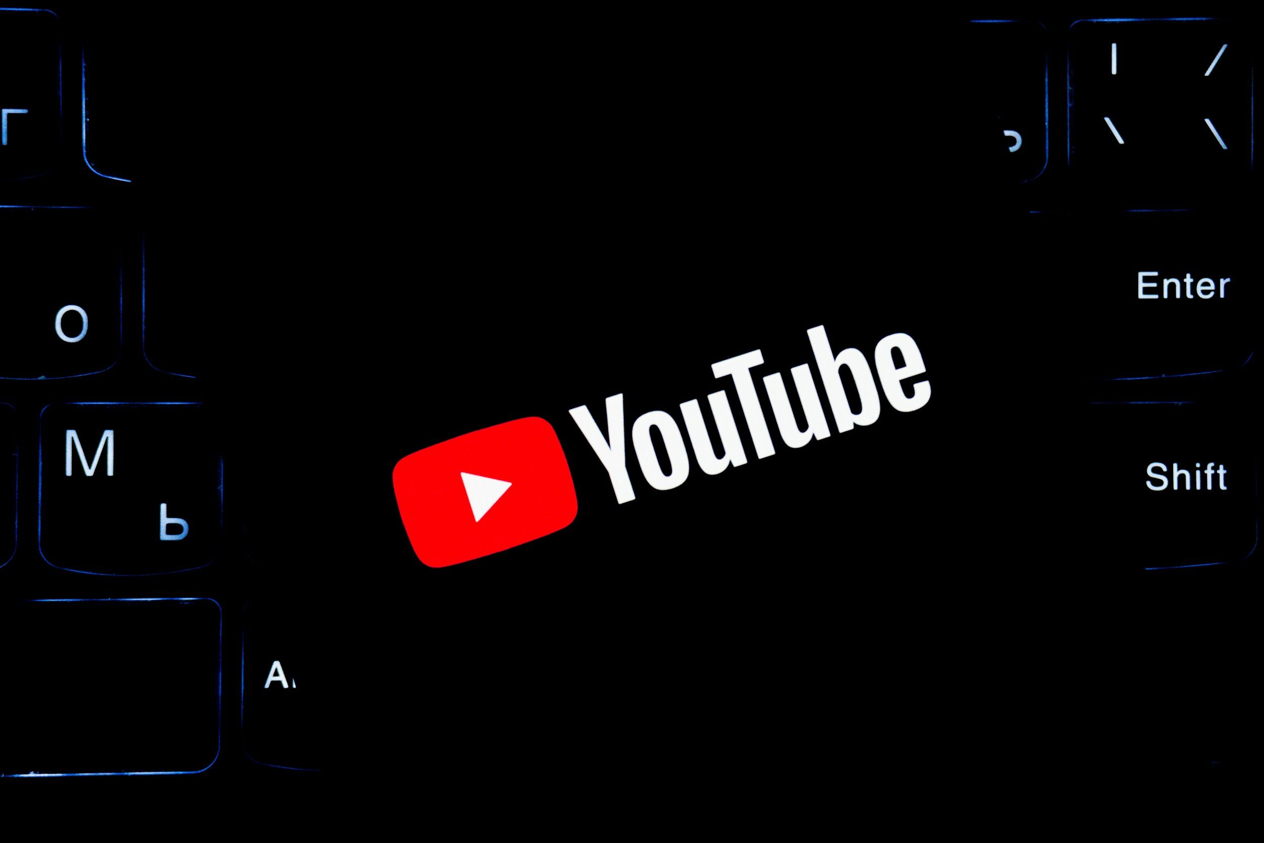 A computer keyboard illuminated with blue backlight shows the YouTube logo, which has a red play button and the word 'YouTube' next to it.