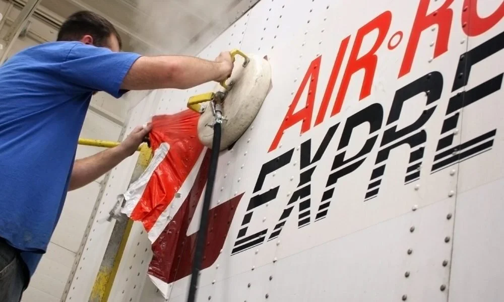 A person cleaning a large white trailer with the logo 'Air Kay Air Express' in red and black.