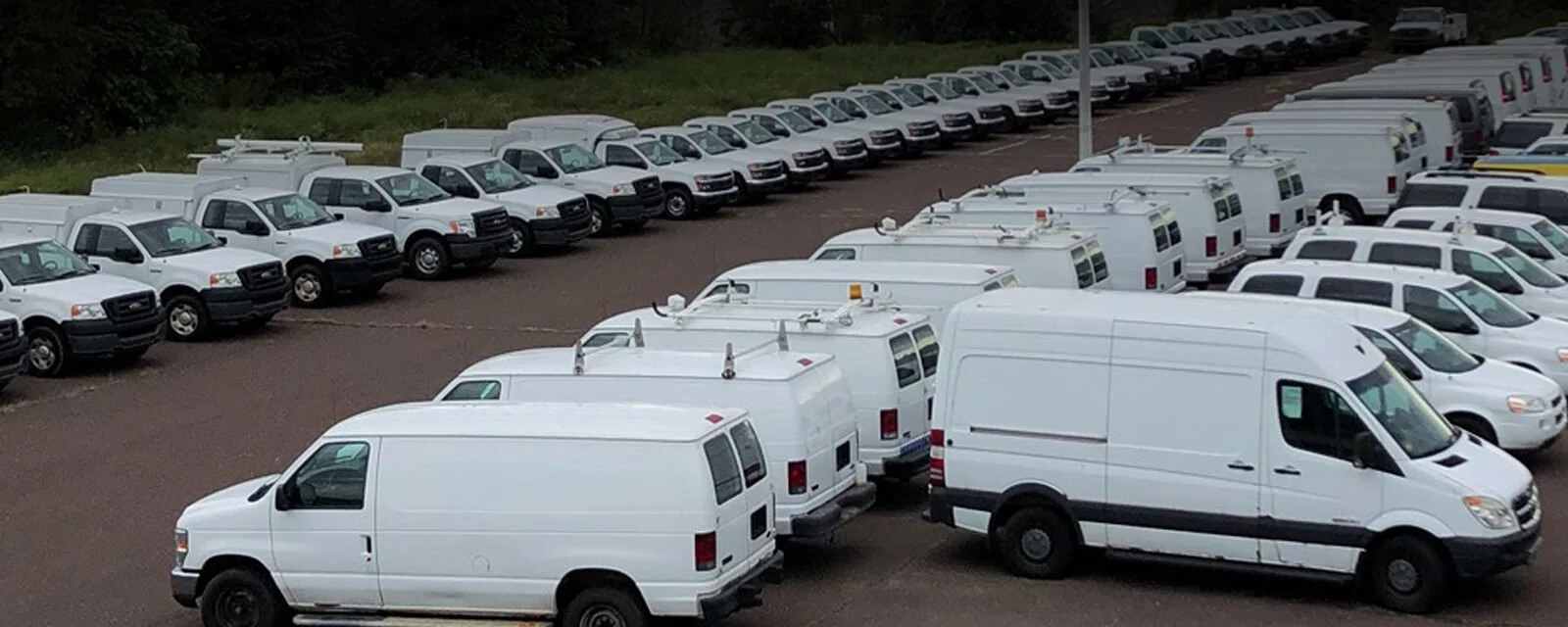 A large parking lot filled with white utility and cargo vans parked in multiple rows.