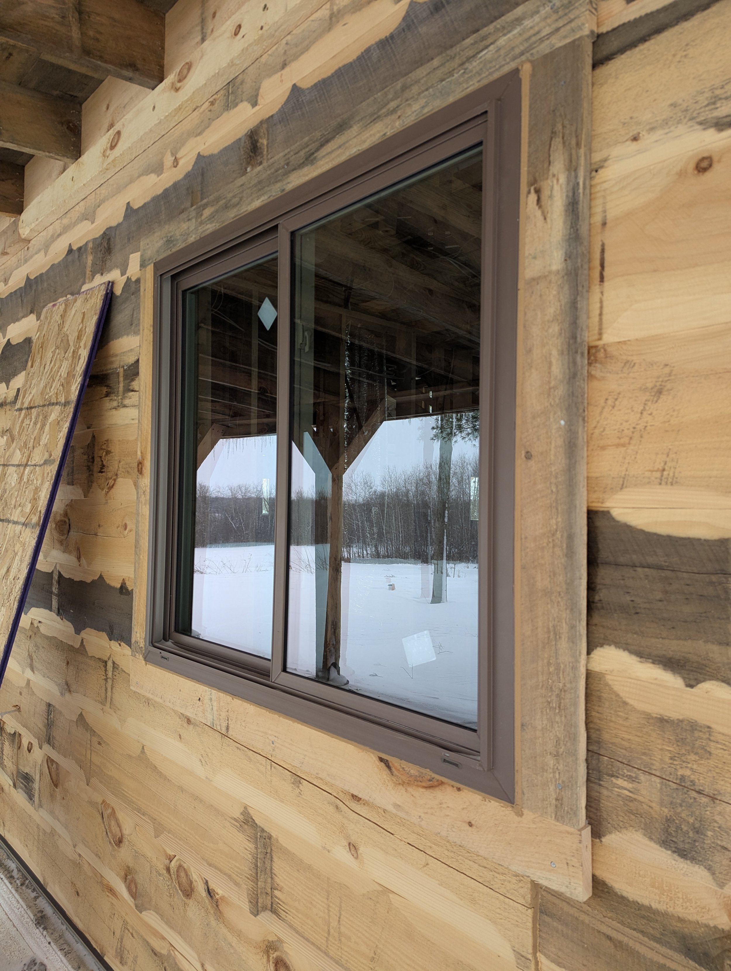 Close-up of a newly installed window on a wooden building with snow outside.