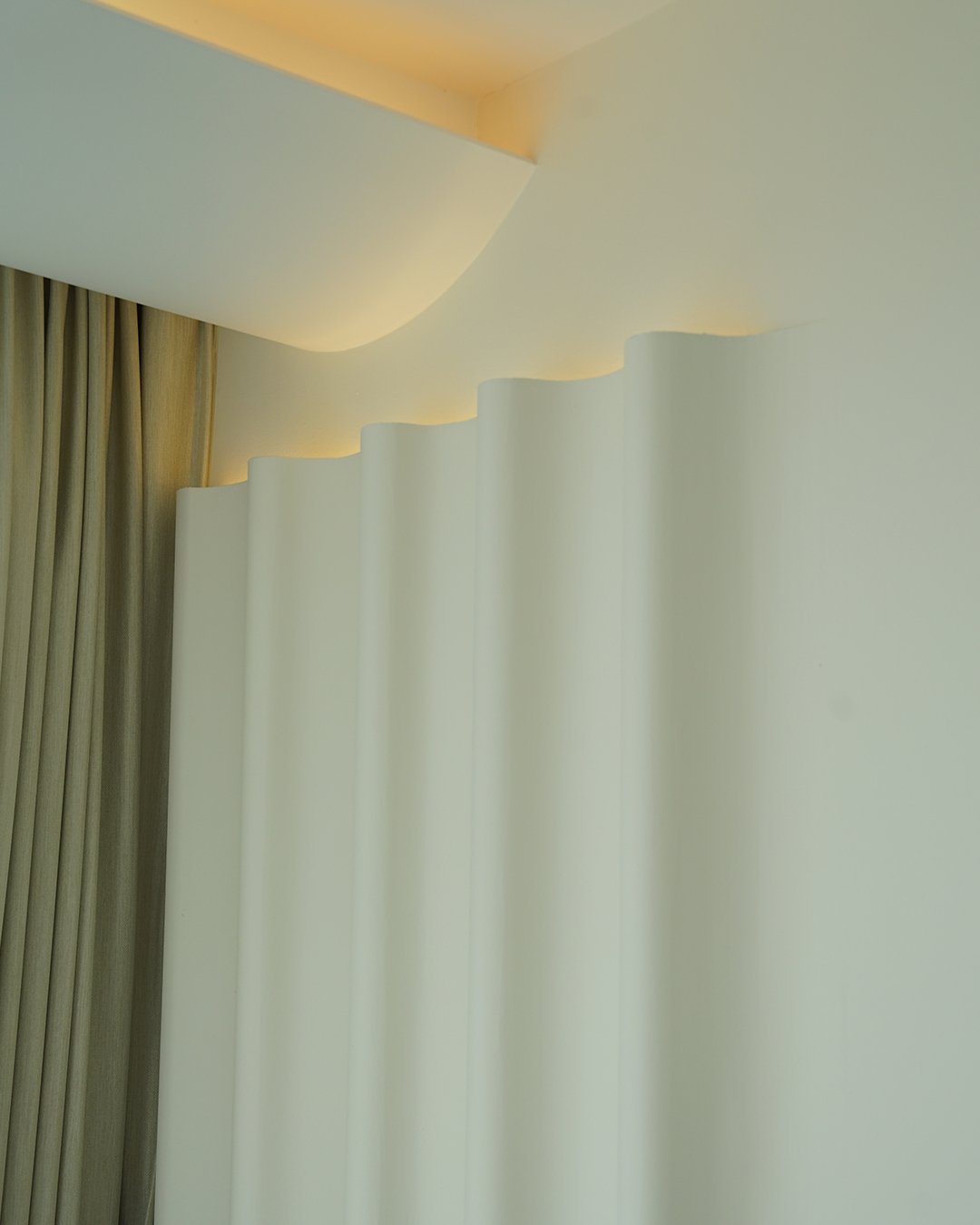Close-up of ceiling with built-in recessed lighting, white ceiling, and white curtains in the background.