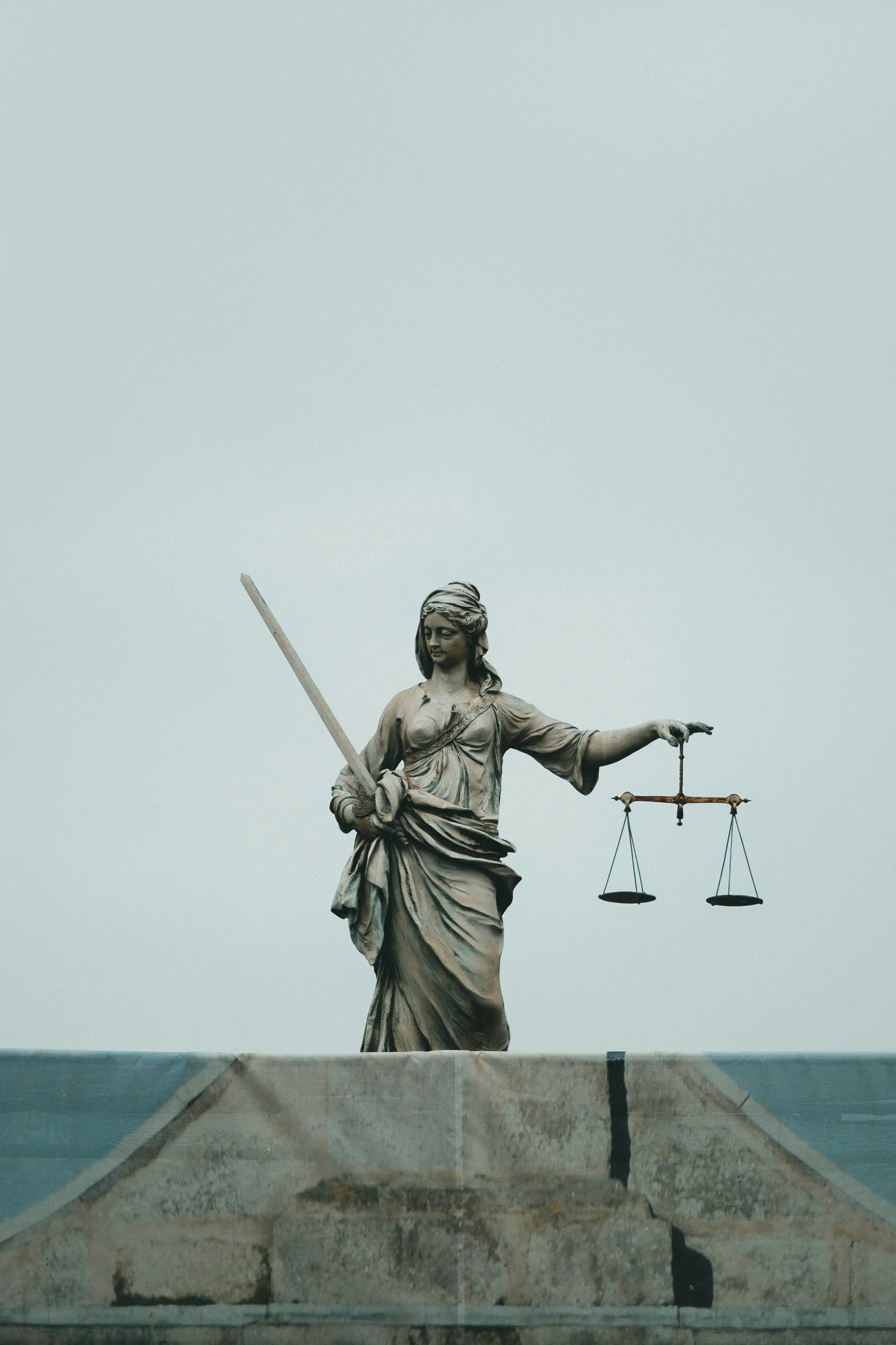 Statue of Lady Justice holding scales in her left hand and a sword in her right hand against a cloudy sky.
