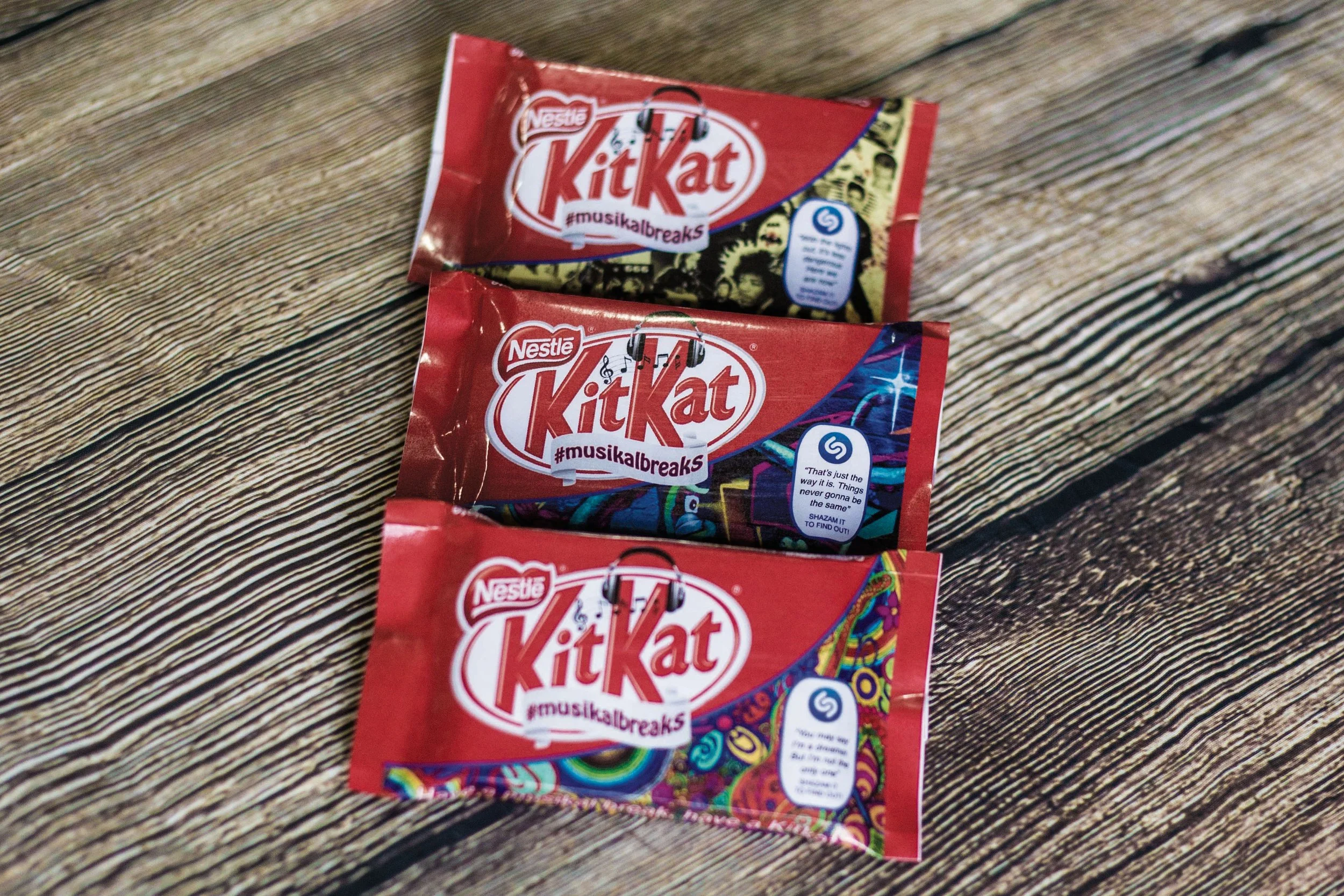 Three Reese's Kit Kat chocolate bars with colorful, musical-themed packaging on a wooden surface.