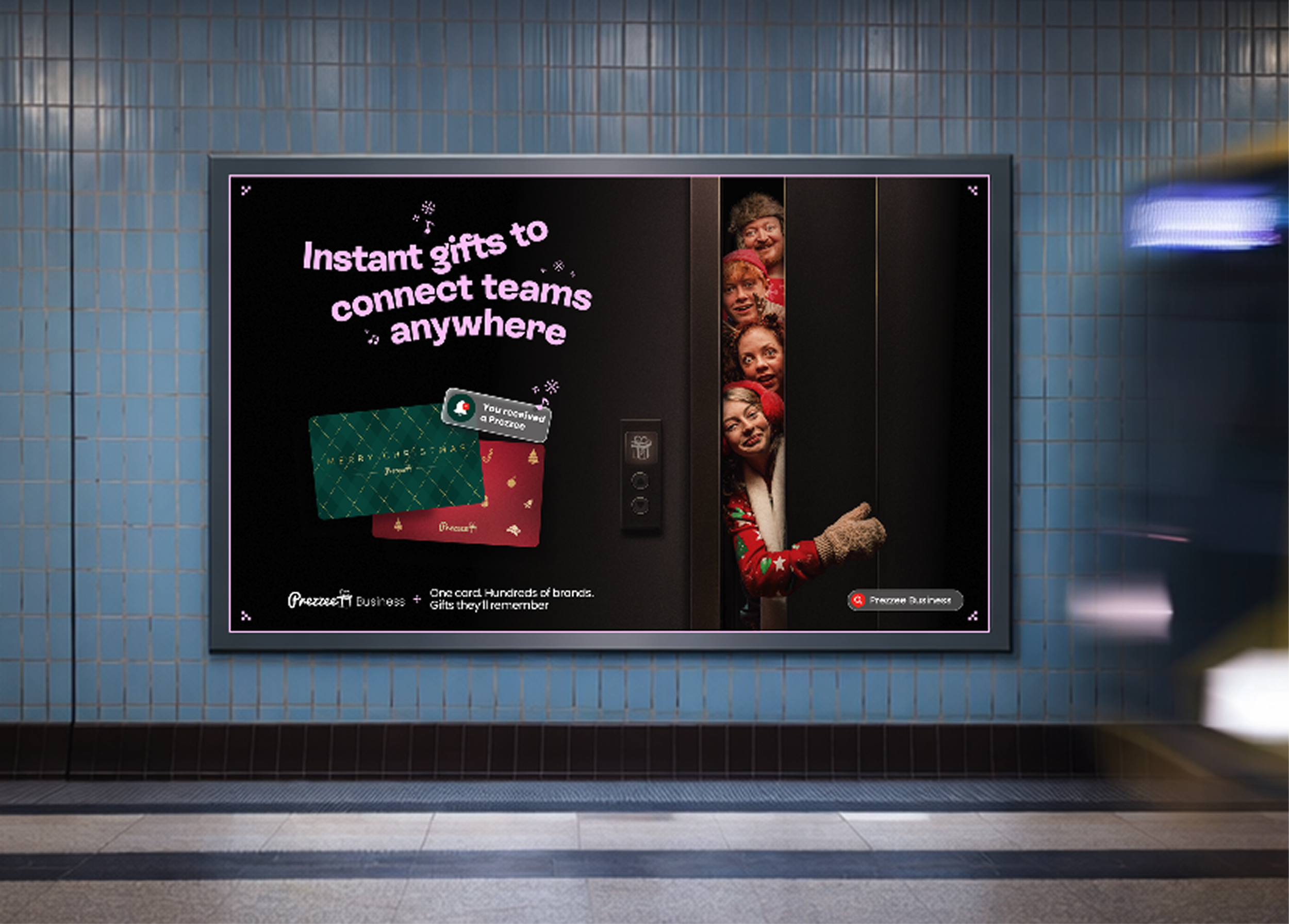 Elevator display screen showing a message about instant gifts connecting teams anywhere, with images of Christmas stockings and a group of people peeking out from elevator doors.