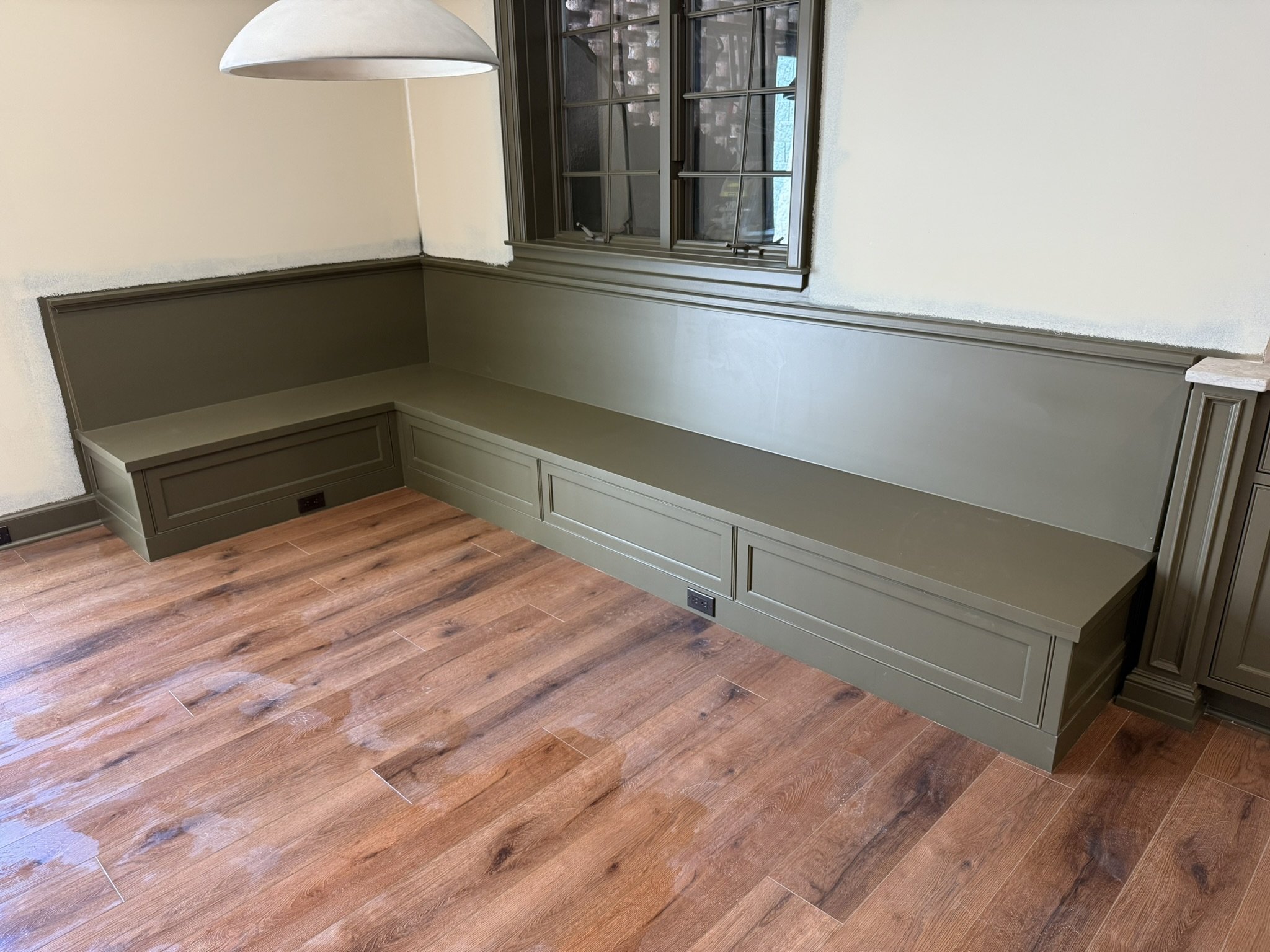 Built-in green bench with storage drawers beneath a window in a room with wood flooring.