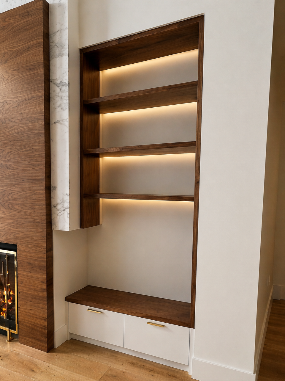 Wooden built-in shelving unit with three open shelves and a drawer at the bottom, located next to a fireplace with a wood mantel.