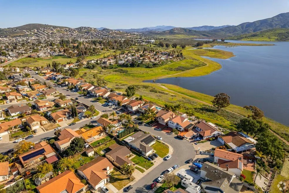 Aerial view of a suburban neighborhood near a large lake with green hills in the background.