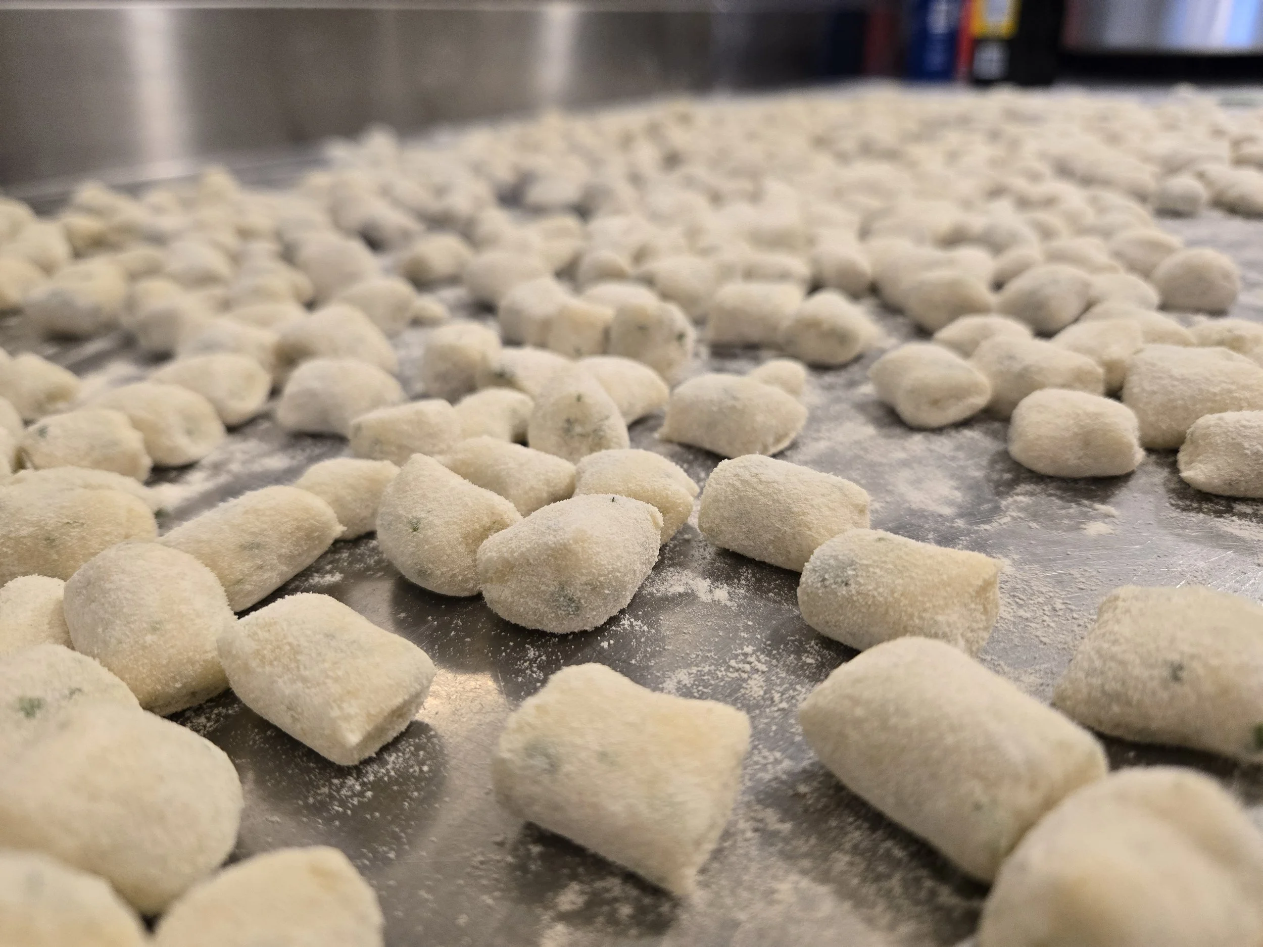 Close-up of small, round, uncooked pasta pieces coated in flour on a metal baking sheet.